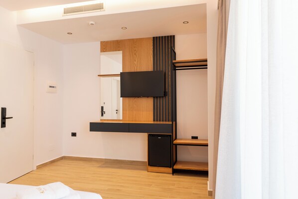 A modern hotel room with a wooden floor, a built-in TV, a small refrigerator, and a wardrobe with a mirror. - Alpaso Hotel (Sarande)