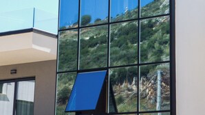 A modern hotel building with a large glass facade reflecting the surrounding landscape. - Alpaso Hotel (Sarande)