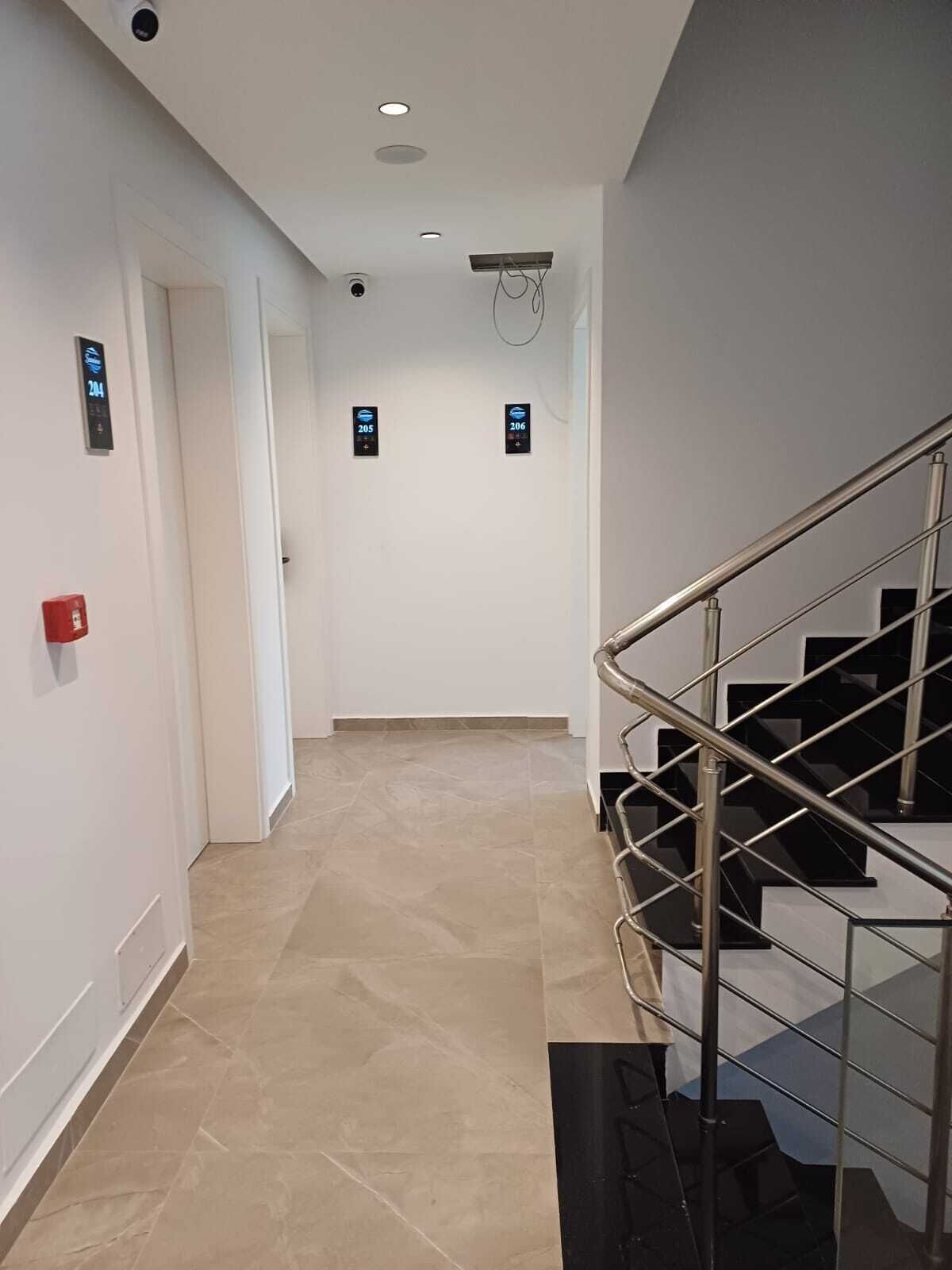 A modern hotel hallway with a staircase, a fire alarm, and digital elevator call buttons.
