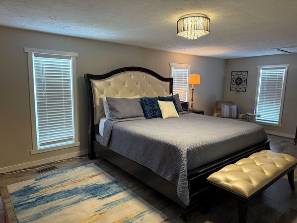 A bedroom with a large bed, a bench, a chandelier, and two bedside tables.