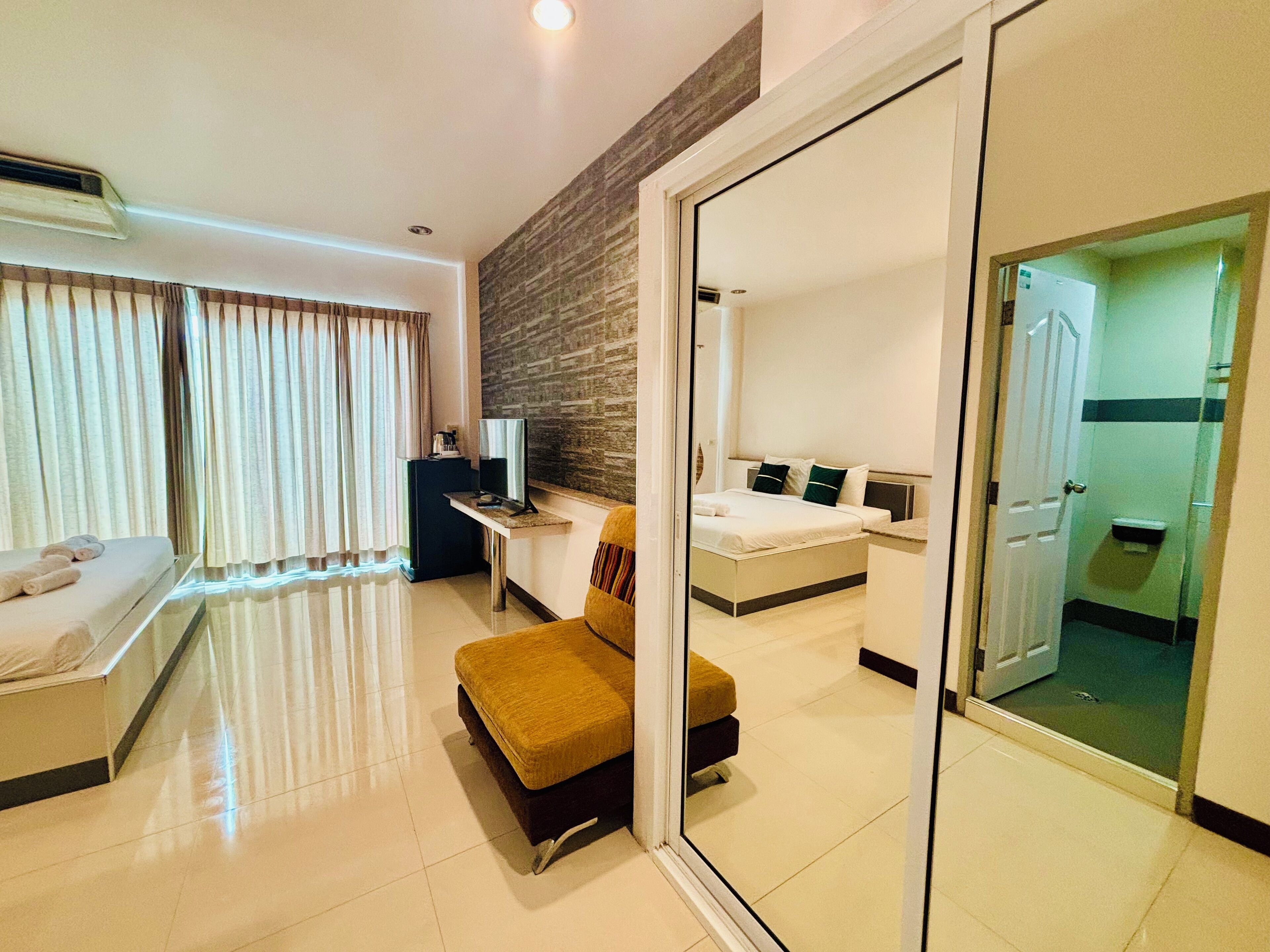 A hotel room with a bed, a desk, a chair, a TV, and a bathroom visible through a glass door.