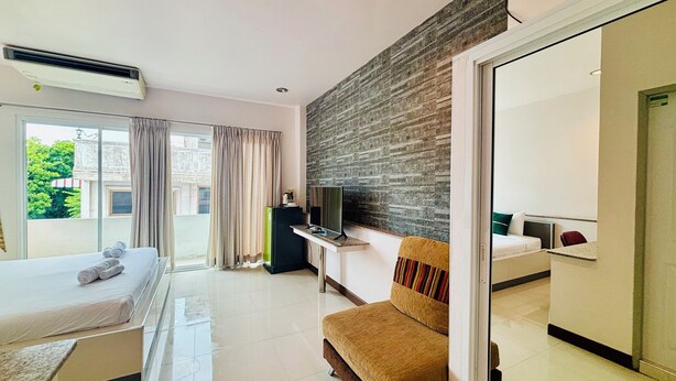 Habitación de hotel con cama, sofá, televisor y balcón con cortinas.