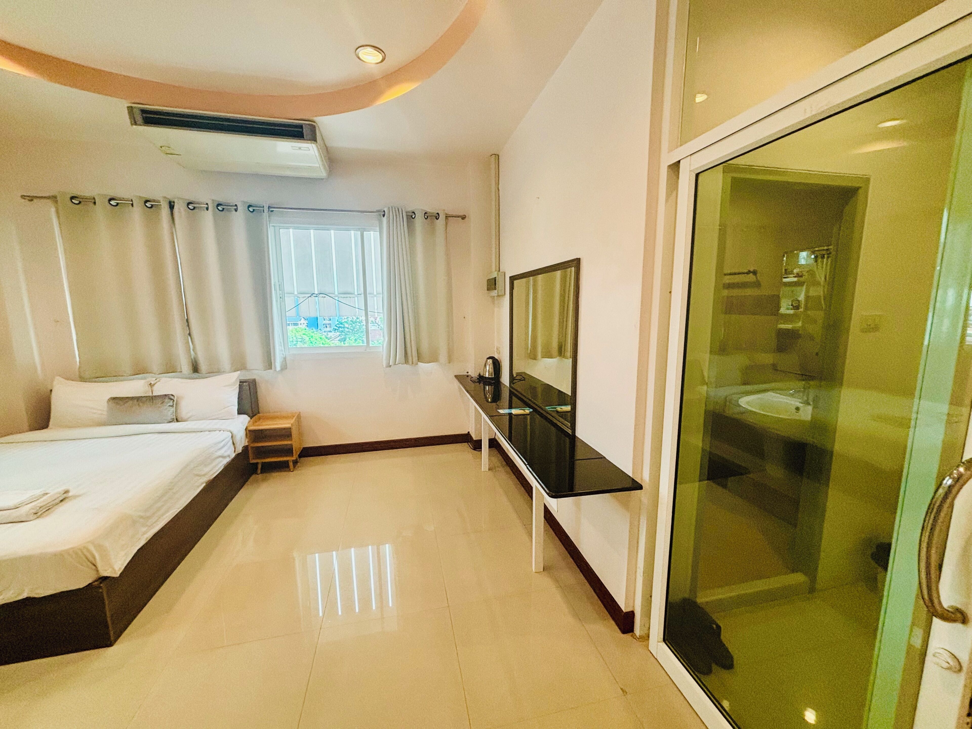 Une chambre d’hôtel avec un lit, une petite table, un miroir et une salle de bain dotée d’une porte en verre.