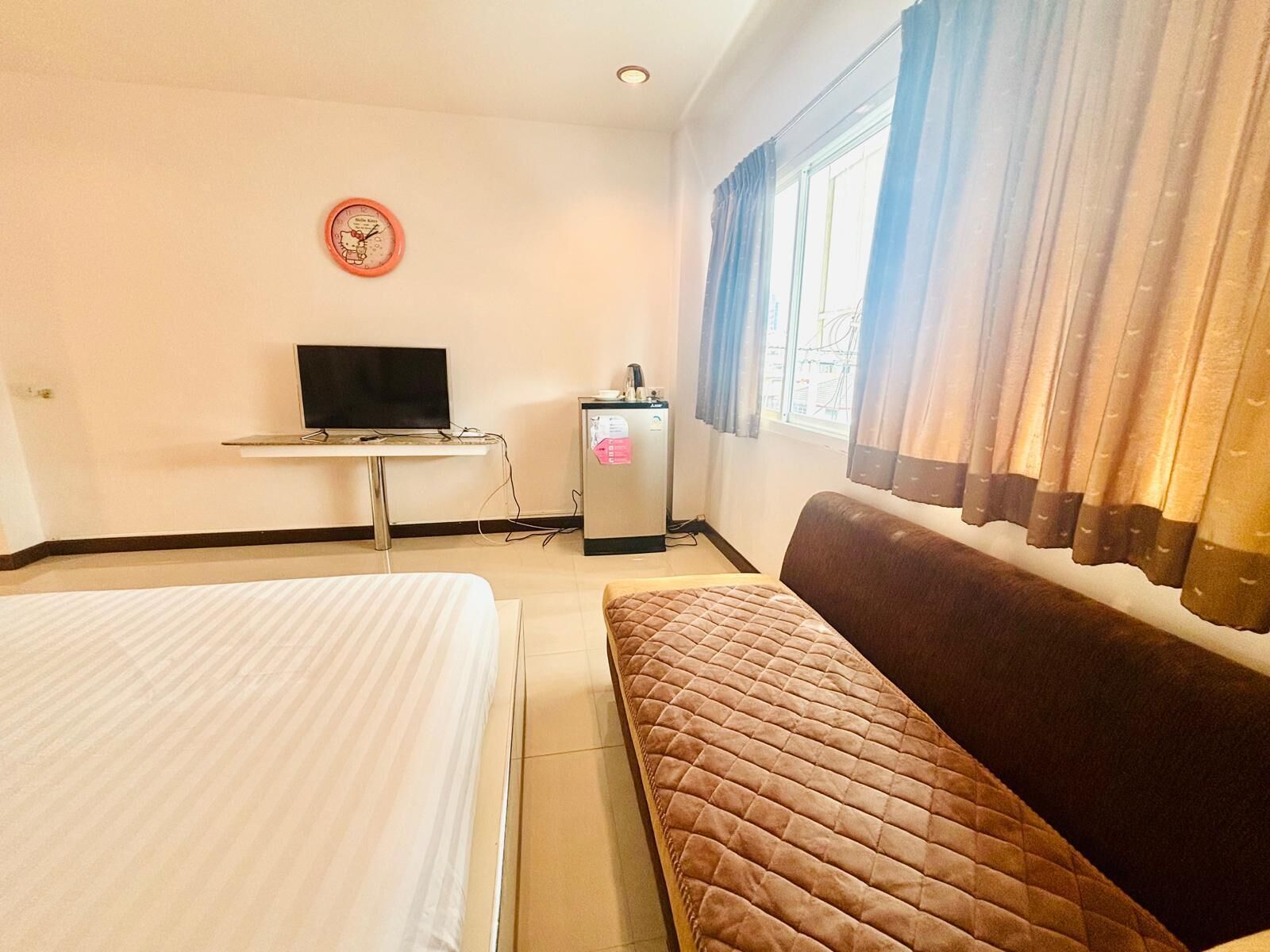 A hotel room with a bed, a sofa, a television, and a refrigerator.