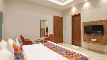 A hotel room with a large bed, two chairs, a small table, a mirror, and a TV mounted on the wall.