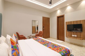 Habitación de hotel con una cama grande, dos sillas, una mesita, un espejo y un televisor montado en la pared.