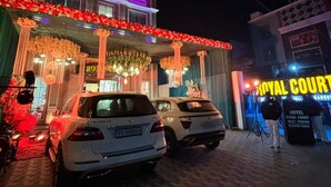 Entrada de un hotel con toldo decorado con flores y luces, y dos coches aparcados.