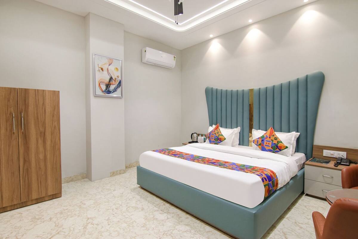 A modern hotel room with a large bed, a wooden wardrobe, a marble floor, and an air conditioning unit on the wall.