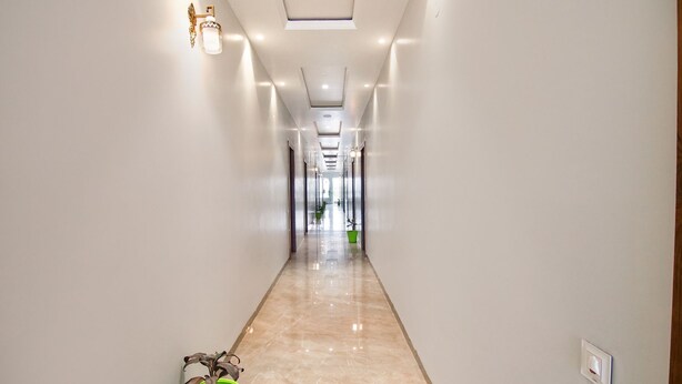 Un pasillo largo y estrecho con piso brillante, una planta verde y un aplique en la pared.