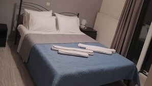 Una cama bien hecha con una colcha azul y almohadas blancas, una mesita de noche con una lámpara, y una pared decorada con motivos florales.