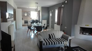 Una sala de estar moderna con sofá, mesa de comedor y sillas. Se observa una cocina al fondo con zona de comedor.