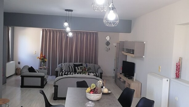 Una sala de estar moderna con comedor, sofás grises, sillas negras y una mesa central con fruta.