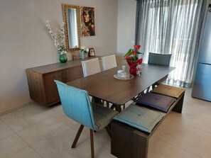 A dining area with a wooden table, blue cushioned chairs, and a bench. There is a mirror on the wall and a painting above the table.