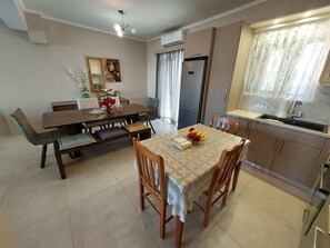 A dining area with a wooden table and chairs, a bench, a mirror, and a refrigerator.