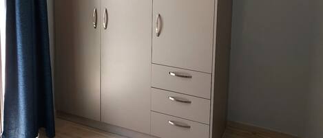 A room with a large wardrobe, a bed with a patterned bedspread, and a window with curtains.