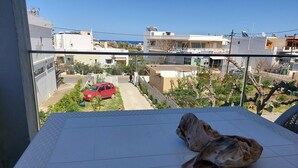 A balcony with a view of a red car parked on the street, a tree, and buildings in the background. - Rethymno Suburb Maisonette (Rethymno)