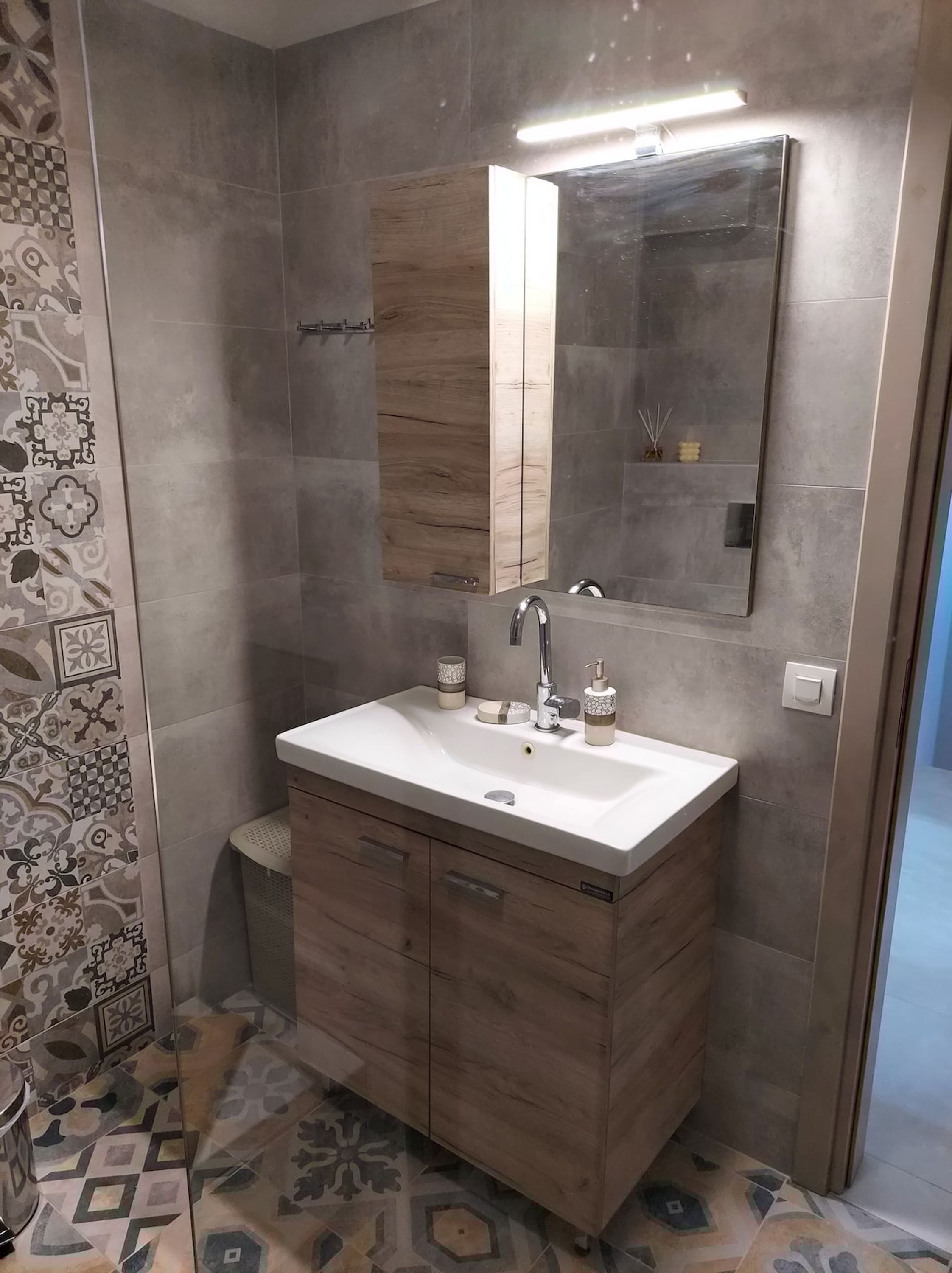 A modern bathroom with a large mirror, a white sink, and a wooden vanity.