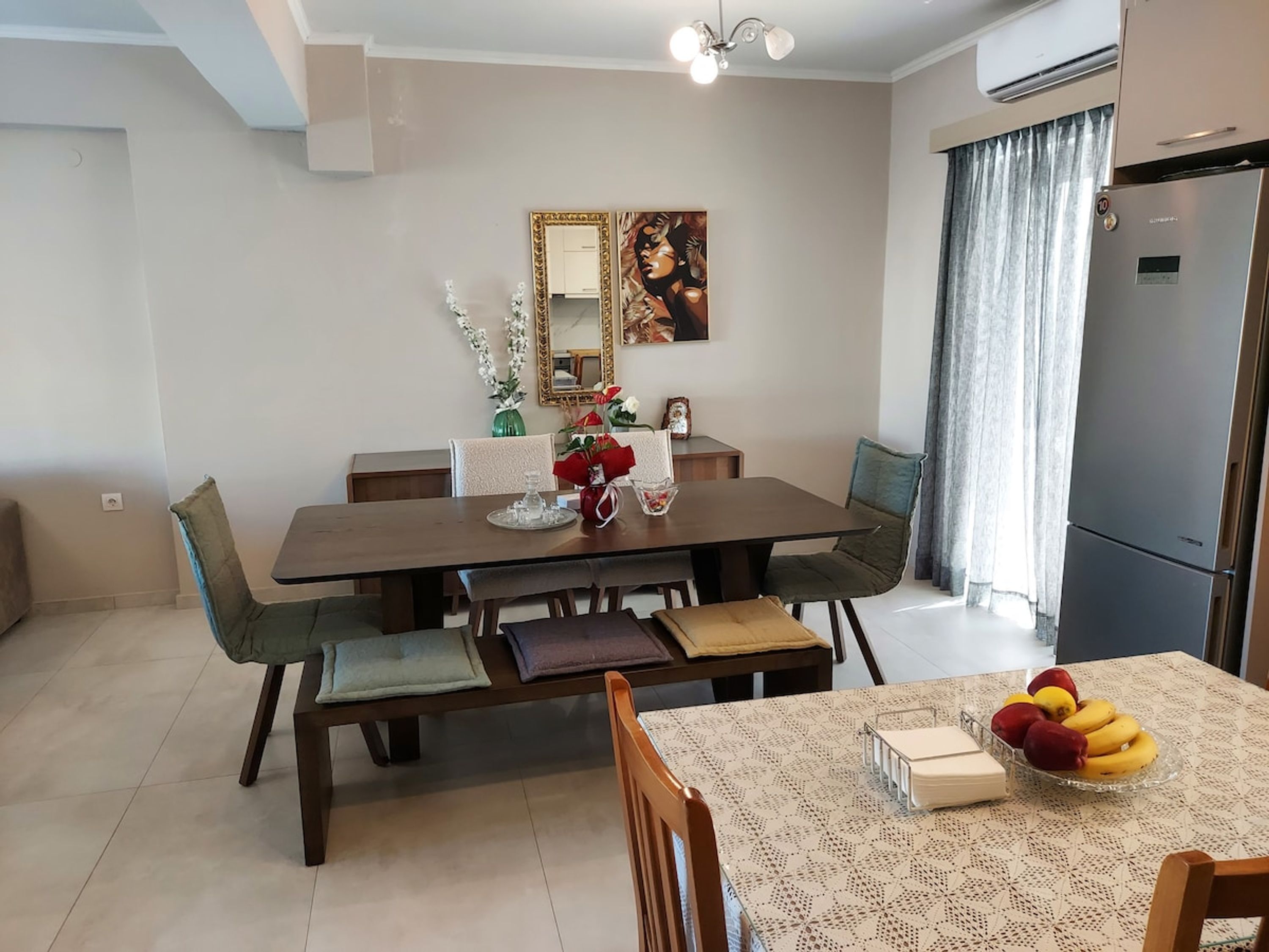 A dining area with a wooden table, chairs, a fruit bowl, and a painting on the wall.