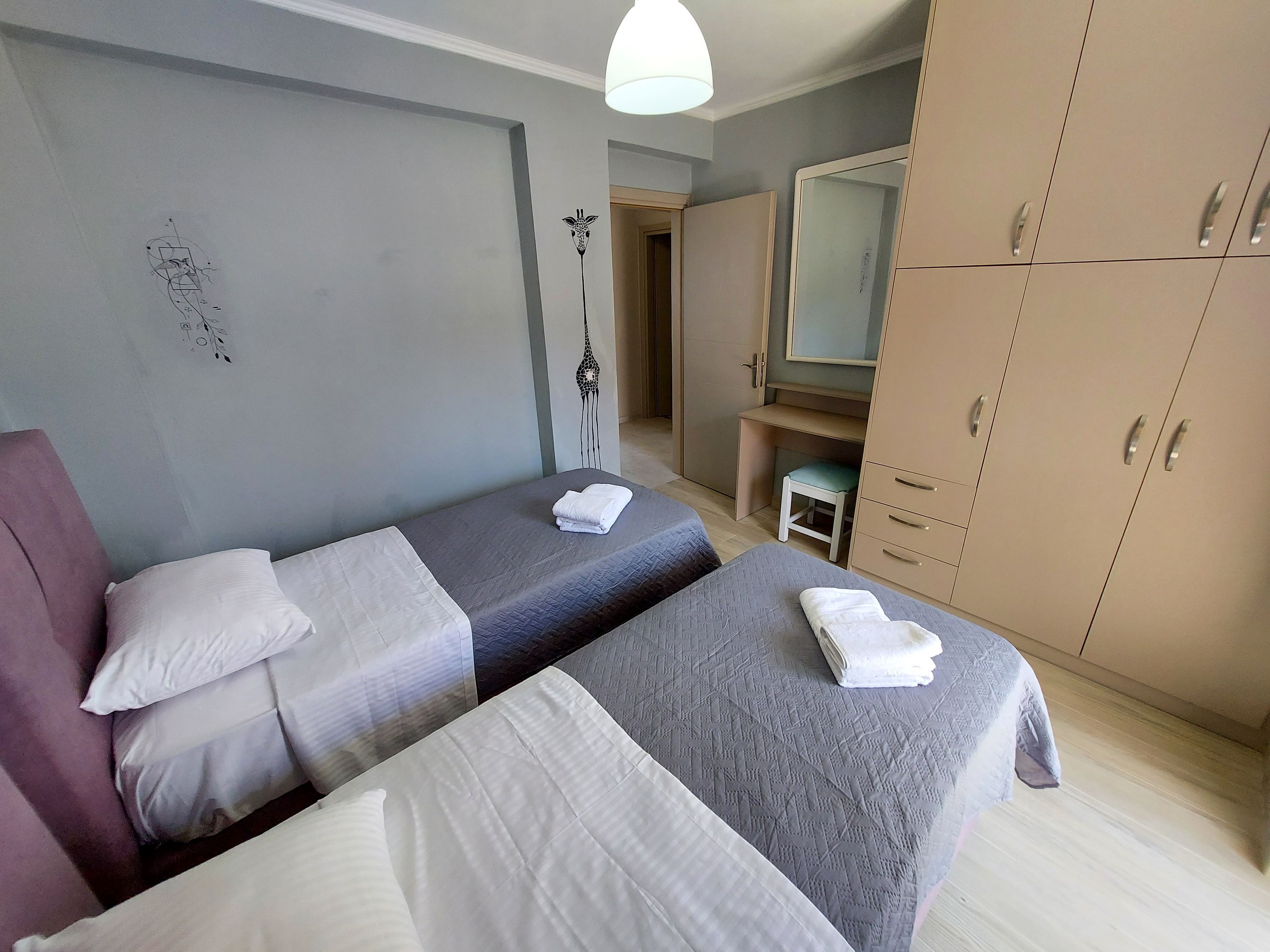 A hotel room with two beds, a wardrobe, a desk, and a mirror.