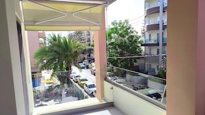 Ein Balkon mit Blick auf eine Straße, eine Palme und ein Gebäude mit Balkonen.