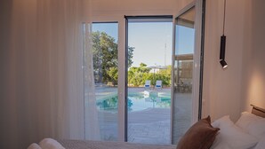 A hotel room with a bed, a view of an outdoor swimming pool, and a sliding glass door. - ng Lique Pool Garden Apartment (Rethymno)