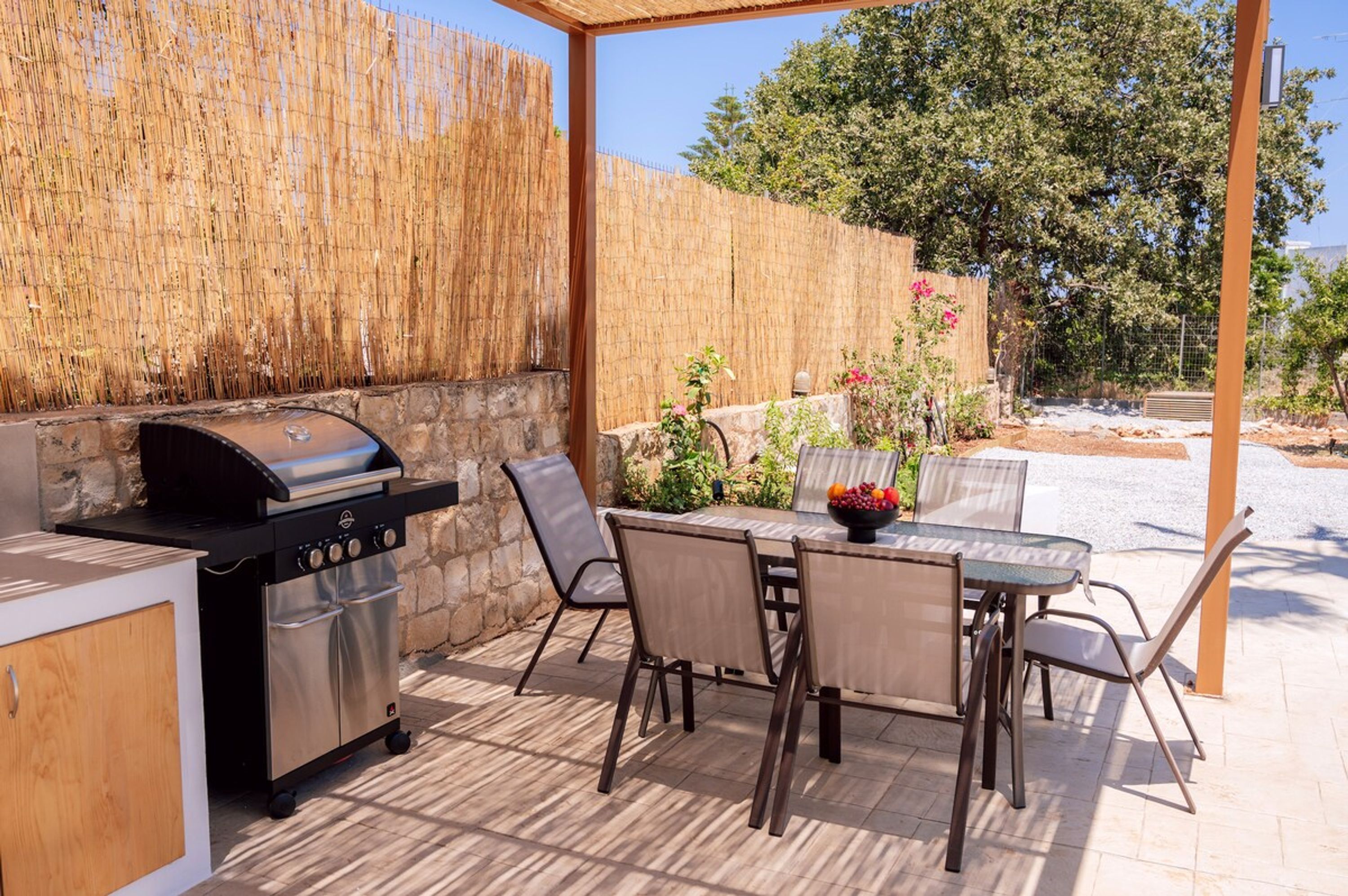 An outdoor patio with a barbecue grill, a table with chairs, and a stone wall.