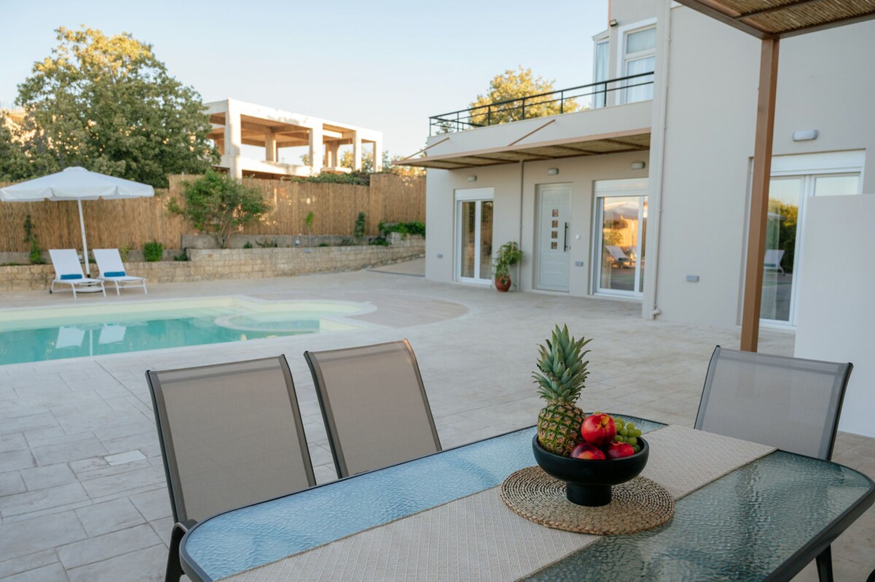 Ein Poolbereich mit Esstisch, Liegestuhl und Blick auf ein modernes Gebäude mit Balkon.