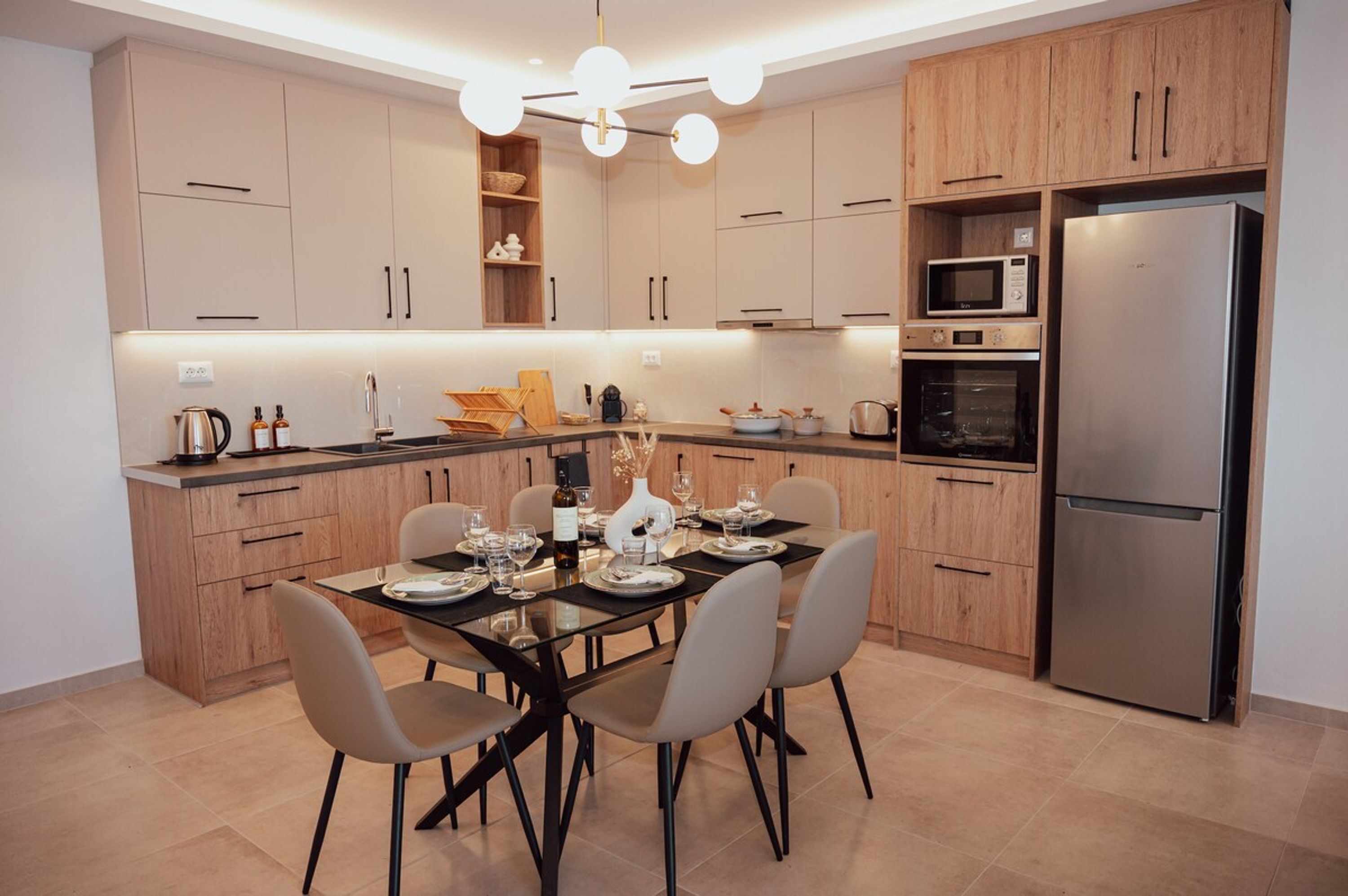 A modern kitchen with wooden cabinets, a stainless steel refrigerator, a microwave, and a dining table set for four.