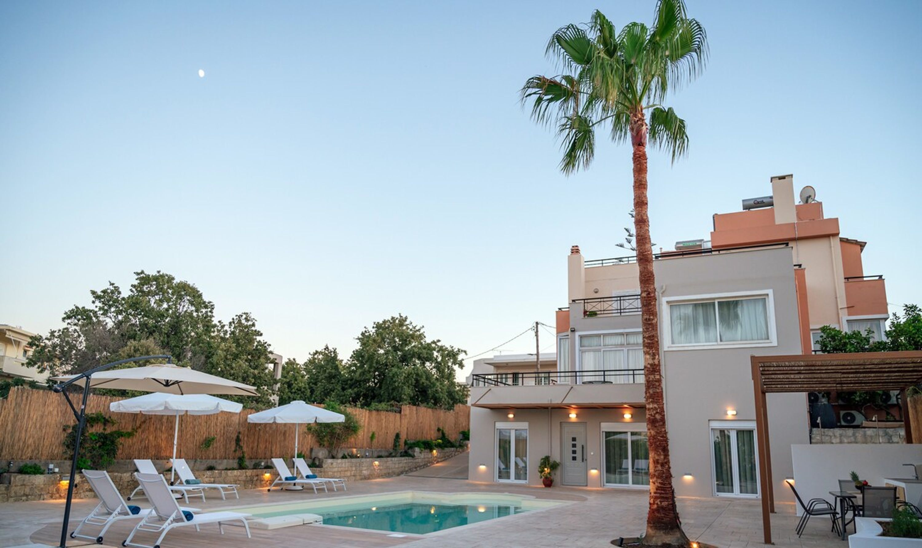 Een modern huis met twee verdiepingen, een zwembad, ligbedden en parasols.