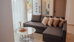 A modern living room with a grey sectional sofa, a round coffee table, and a large mirror. - ng Lique Pool Garden Apartment (Rethymno)