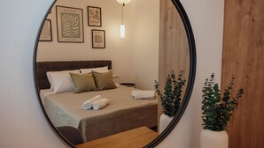 A bedroom with a bed, pillows, a bedside table, a mirror, and framed artwork on the wall. - ng Lique Pool Garden Apartment (Rethymno)