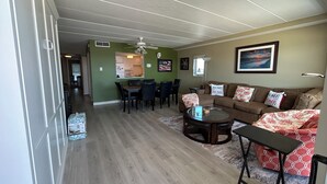 Una sala de estar con un sofá marrón, una mesa de centro de vidrio y un comedor con una cocina al fondo.