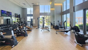 Une salle de sport spacieuse équipée de machines de cardio, de matériel de musculation et de grandes fenêtres offrant une vue sur l’extérieur.