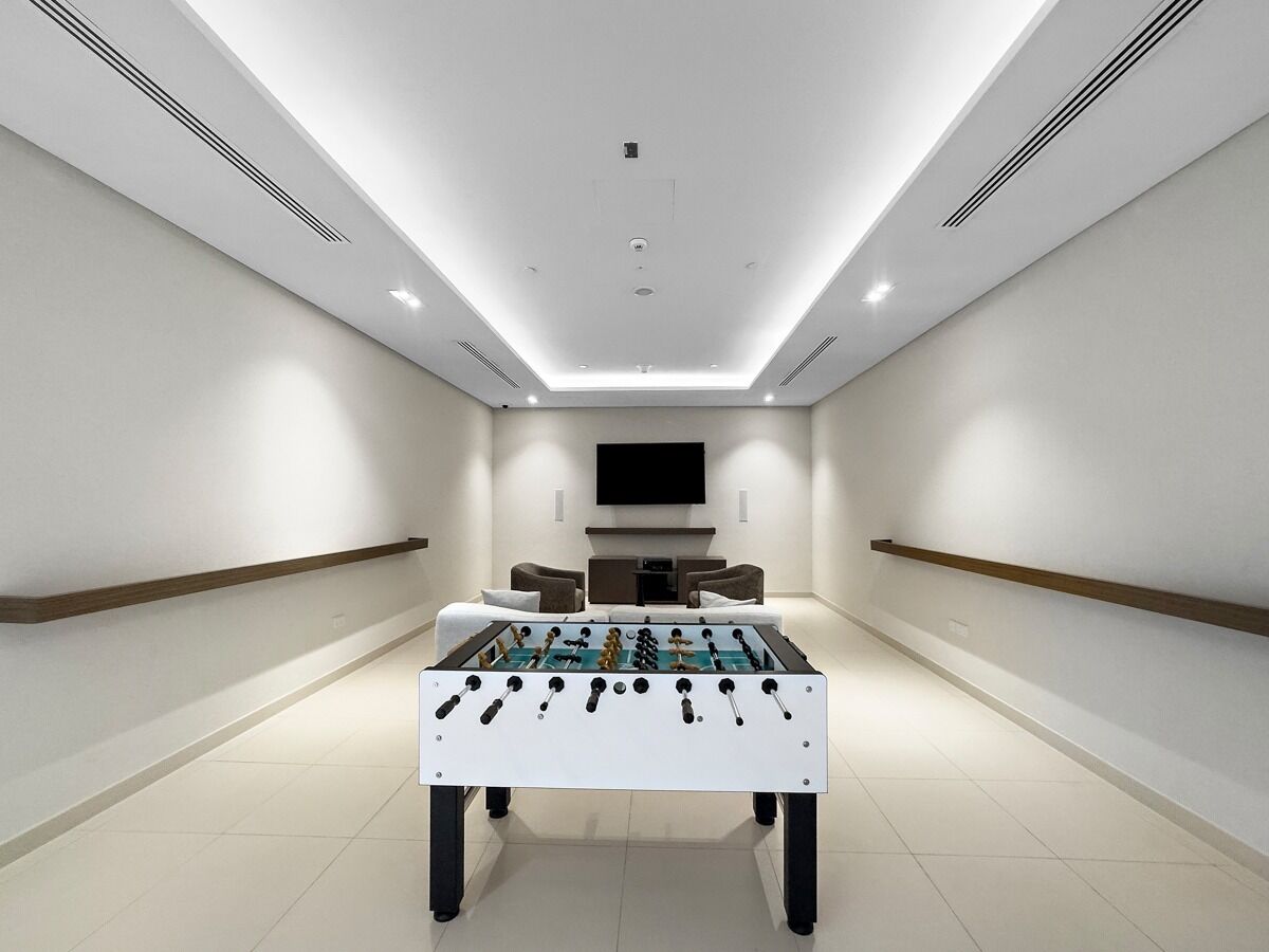 A modern, well-lit room with a foosball table, a flat-screen TV mounted on the wall, and a seating area with sofas.
