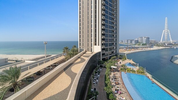 Un hôtel de grande hauteur doté d’une piscine et offrant une vue sur la plage, avec une grande roue en arrière-plan.