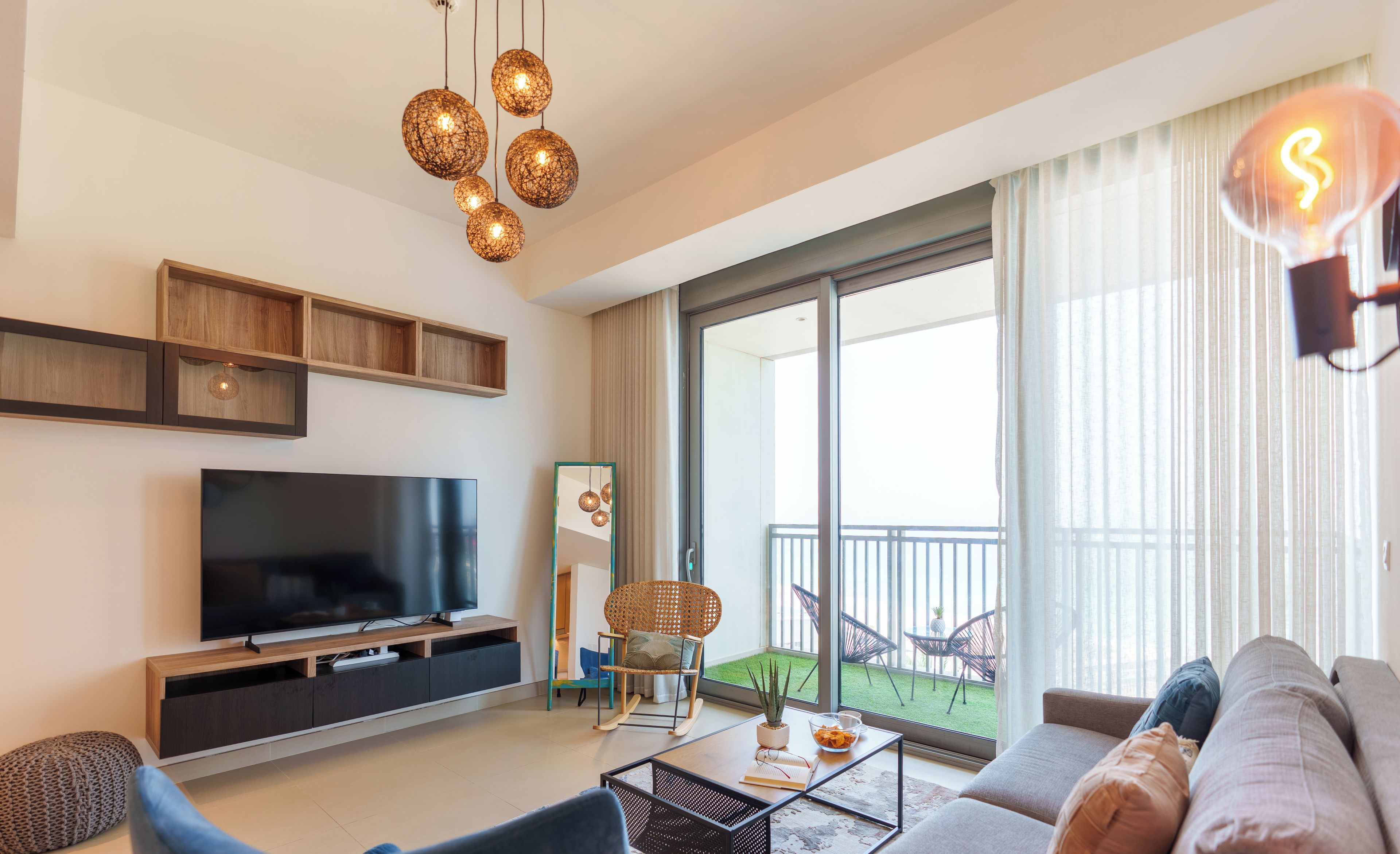 Een moderne woonkamer met een flatscreen televisie, een bank, een salontafel en een balkon met tuinmeubilair.