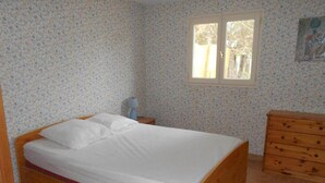 A bedroom with a wooden bed, a dresser, a window, and floral wallpaper. - 8 pers, 200m from the sea, garden, ground floor, closed private parking, independent entrance (Marseillan)