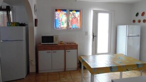 A compact kitchen with white cabinets, a microwave, and a refrigerator. There is a small table with a yellow tablecloth and a window with colorful stained glass above it. - 8 pers, 200m from the sea, garden, ground floor, closed private parking, independent entrance (Marseillan)
