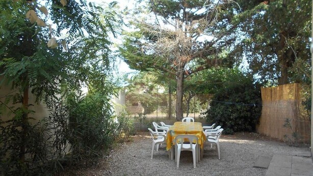 A gravel patio with a round table and chairs, surrounded by dense foliage and a wooden fence. - 8 pers, 200m from the sea, garden, ground floor, closed private parking, independent entrance (Marseillan)