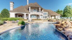 Une grande maison avec une piscine, des piliers en pierre et un mur en pierre.