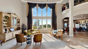 Un salon spacieux avec une grande fenêtre, un coin repas et un hall doté d’un plafond haut.