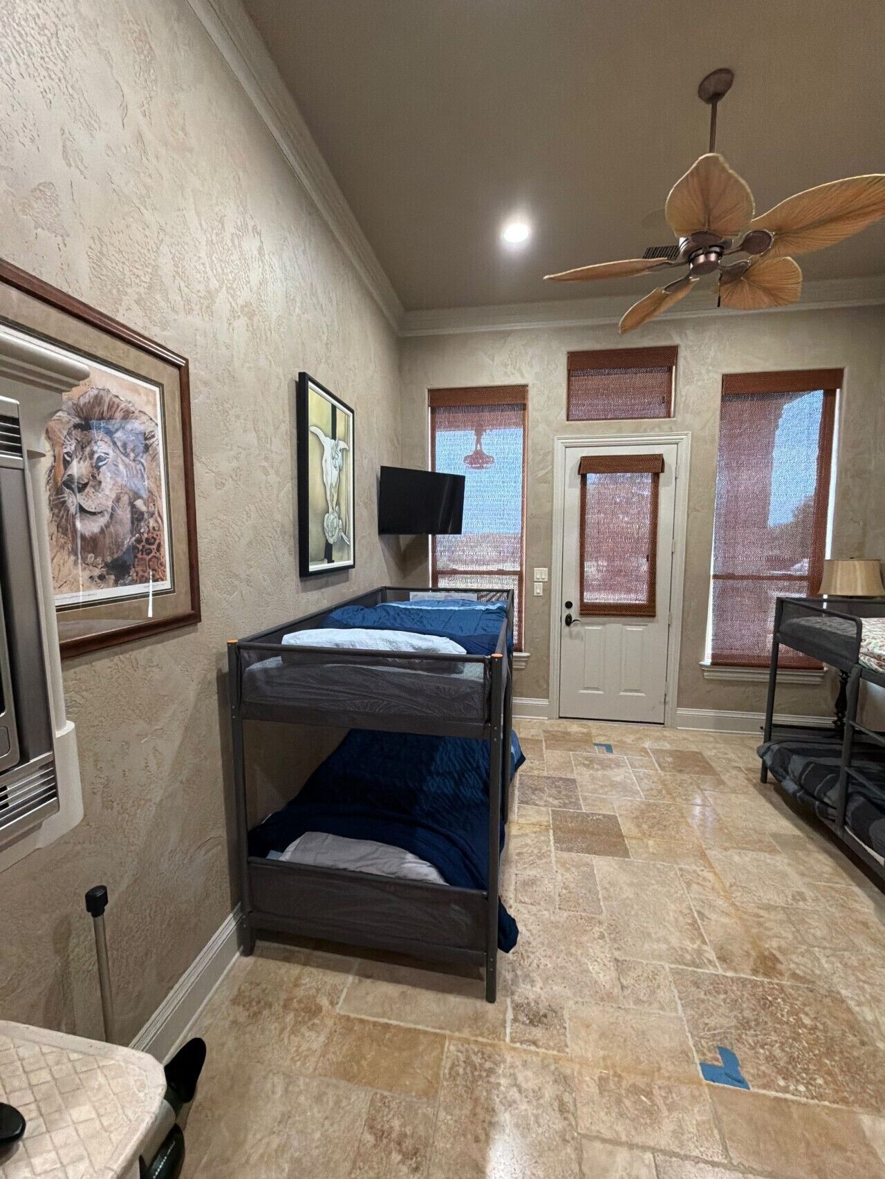 A room with bunk beds, a ceiling fan, a television, and artwork on the walls.