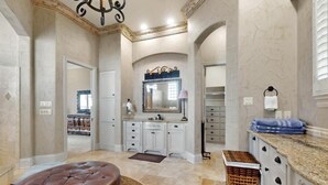 Une salle de bain spacieuse, dotée d’un grand meuble-lavabo, d’un miroir et d’un coin salon.
