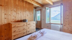 A wooden-paneled bedroom with a bed, a wooden dresser, and a window with a mountain view.