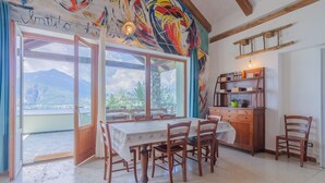 A dining area with a table and chairs, a wooden cabinet, and a view of mountains through large windows.