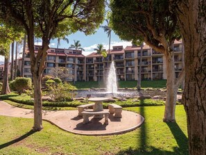 Un patio con una fuente, una mesa de piedra y bancos rodeados de árboles.