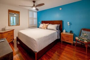 Un dormitorio con cama, cómoda de madera, mesita de noche, silla y ventilador de techo.