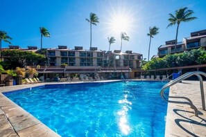 Una piscina con agua azul cristalina, rodeada de palmeras y un edificio de varios pisos con balcones.