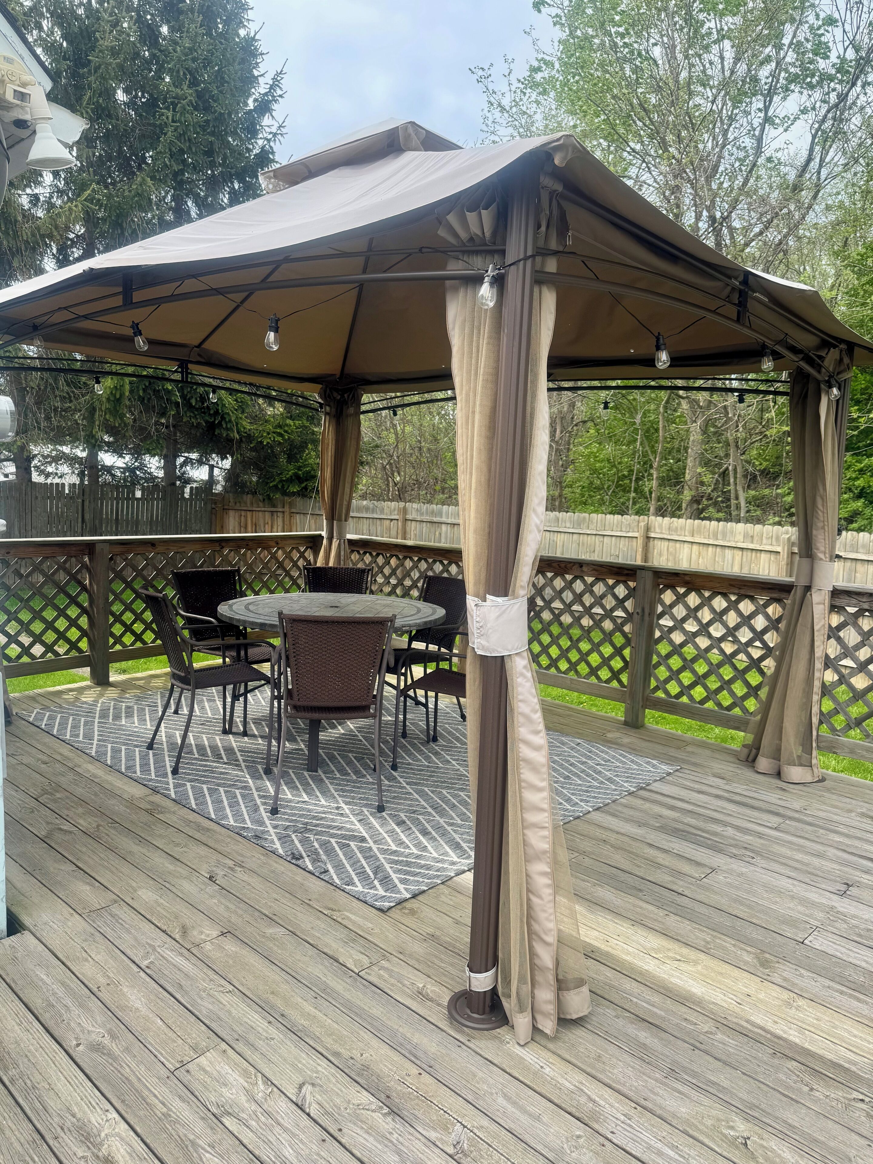Eine überdachte Terrasse im Freien mit Tisch und Stühlen, umgeben von einer Holzterrasse und einem Holenzaun.