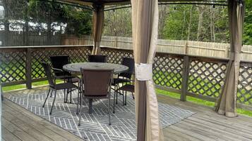 Une terrasse extérieure couverte, dotée d’une table et de chaises, entourée d’une terrasse en bois et d’une clôture en bois.